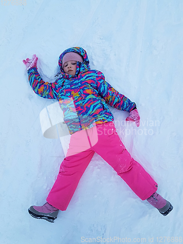 Image of Cute little kid girl in warm ski sport suit making snow angel outdoors. Kid having fun lying on snowdrift after snow storm in winter. Children outdoor activities. Winter vacation and holidays.