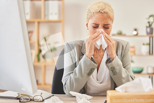 Image of Computer, tissue and a business woman blowing nose while working at a desk, sick in the office. Cold, flu or symptoms with a young female corporate employee sneezing from hayfever allergies at work