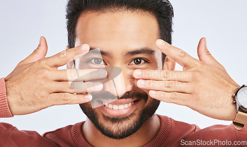 Image of Portrait, smile and asian man with fingers on eyes in studio with confidence, personality and persona on grey background. Hands, happy and male person with hand gesture for mask, masquerade or silly