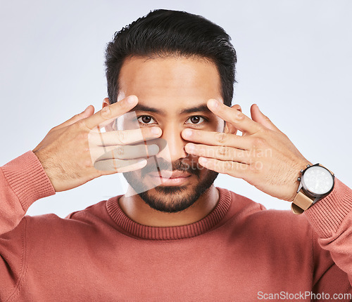 Image of Portrait, eyes and asian man with fingers on face in studio with confidence, personality and persona on grey background. Hands, pose and male person with hand gesture for mask, masquerade or ego