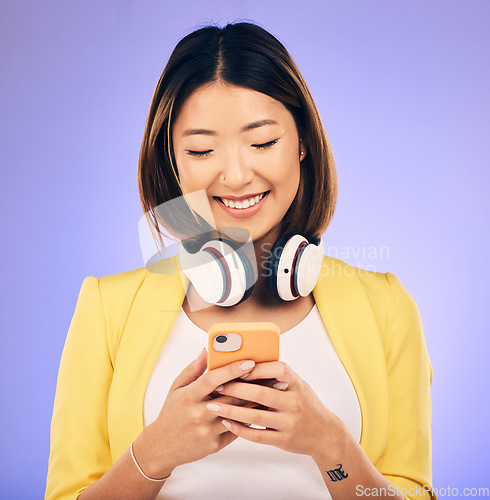 Image of Social media, phone and happy Asian woman in studio for text message, internet meme and chat. Headphones, smile and female person on smartphone listen to audio, song and track on purple background