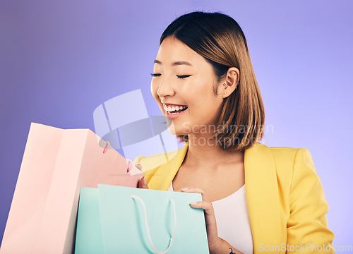 Image of Check, shopping bag and young woman for fashion sale, discount or retail prize on studio, purple background. Excited model, asian person or happy customer with choice, giveaway and wealth or gift