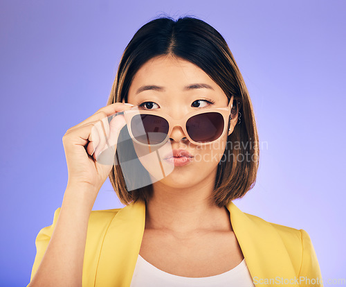 Image of Fashion, sunglasses and a model asian woman on a purple background in studio for trendy style. Face, shades and attitude with a confident young female person looking over a stylish eyewear frame