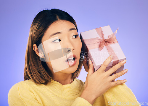 Image of Thinking, gift and box with face of asian woman in studio for birthday, celebration and curious. Surprise, wow and party with female person and present on purple background for giveaway and package