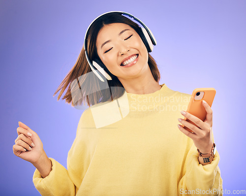 Image of Dance, music and happy Asian woman with phone in studio for streaming, subscription and radio. Relax, headphones and female person on smartphone listen to audio, song and track on purple background