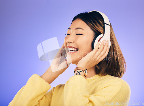 Image of Happy asian woman, headphones and listening to music for online streaming against a purple studio background. Female person or model smile enjoying audio track, sound or songs on headset on mockup