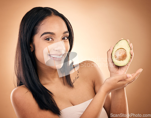 Image of Face, smile and woman with avocado for skincare isolated on a brown background in studio. Portrait, fruit and model with food for nutrition, skin health and vegan diet, vitamin c or natural cosmetics