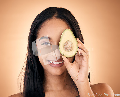 Image of Happy, face and woman with avocado for skincare isolated on a brown background in studio. Portrait, fruit and model with food for nutrition, skin health and vegan diet, omega 3 or natural cosmetics