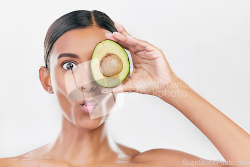 Image of Woman, avocado and funny studio portrait for health, wellness and diet for facial glow by white background. Girl, model and fruit for skincare, nutrition or cosmetics with comic expression for beauty