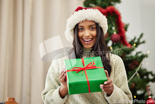 Image of Christmas, portrait or happy girl with a gift box or present on a holiday celebration at home in winter. Guessing, smile or excited Indian woman with package with festive or xmas parcel in a house