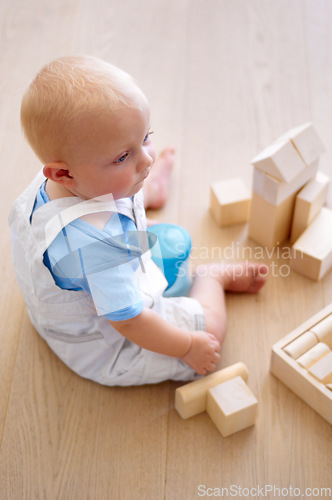 Image of Little baby boy, toys and wooden blocks on floor for playtime, learning or childhood development at home. Cute, adorable or growing infant of newborn, child or toddler playing on the ground in house