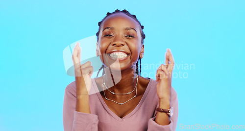 Image of Face, fingers crossed and black woman with smile, hope and motivation with lady against blue studio background. Portrait, African American female and girl with gesture for luck, wish and emoji sign