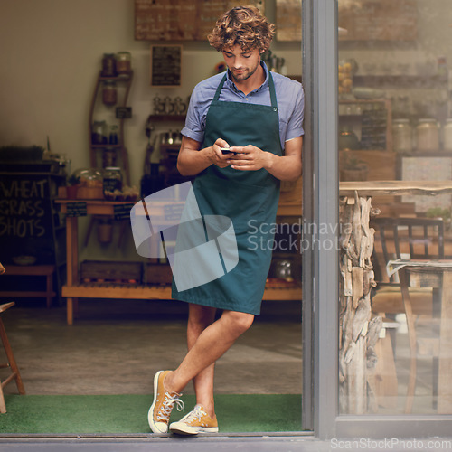 Image of Coffee shop, typing and phone of a man as a small business owner at front door. Entrepreneur person as barista, manager or waiter in restaurant with mobile app for service, marketing or communication