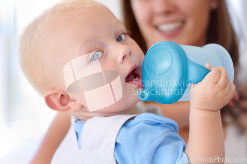 Image of Portrait, family and a baby boy drinking water from a bottle with his mother in the blurred background. Face, kids and hydration with a young child in his home for a drink during child development