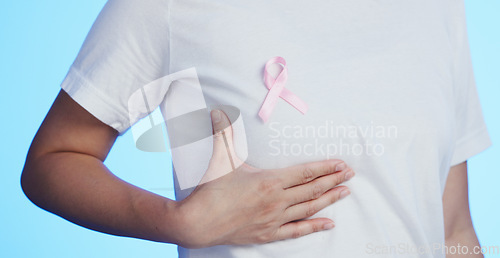 Image of Pink ribbon, breast cancer and awareness with a woman in studio on a blue background for health. Chest, medical and healthcare with a female placing a bow, symbol or sign of recognition in october