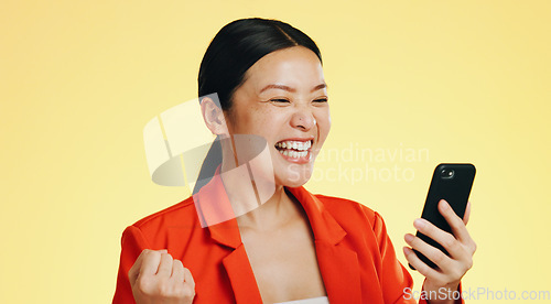 Image of Winner, success celebration and Asian woman with phone in studio isolated on a yellow background. Surprise, fist pump or happy female with mobile to celebrate after winning lottery prize or good news