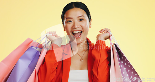 Image of Happy, face and woman in studio with shopping, bag and boutique sale on yellow background. Portrait, excited and asian girl shopper customer with items for discount, fun and retail while isolated