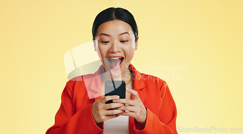 Image of Winner, success celebration and Asian woman with phone in studio isolated on a yellow background. Surprise, fist pump or happy female with mobile to celebrate after winning lottery prize or good news