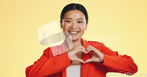 Image of Smile, heart in hands and face of Asian woman on yellow background for love, support and charity mockup. Emoji, hand gesture and portrait of happy girl in studio with shape for care, trust and kind