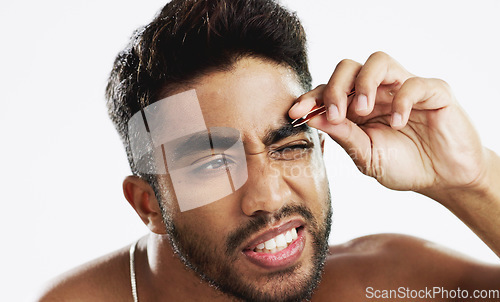 Image of Man grooming his eyebrows with a tweezer in studio for self care, beauty and cleanliness. Hair removal, tweezing and male model from India doing facial epilation plucking routine by white background.