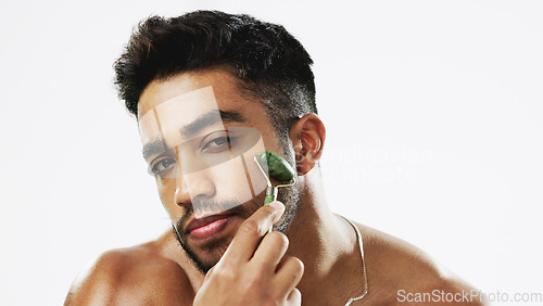 Image of Face, man and facial roller for skincare, cosmetics and wellness against a grey studio background. Portrait, male and guy with rose quartz, massage and salon treatment for smooth, soft and clear skin