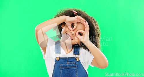 Image of Green screen, happy and child with hands by eyes for glasses gesture for playing, happiness and fun. Emoji face, smile and portrait of girl with funny, comic and humour facial expression in studio