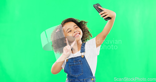 Image of Phone, selfie and child peace sign in a studio with happiness from profile picture. Isolated, green background and young girl with technology showing a v hand gesture for social media with a smile