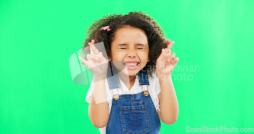 Image of Fingers crossed, wish and praying with girl in studio for good luck, hope and optimism. Excited, emoji and closed eyes with child isolated on green background for miracle, positive and youth