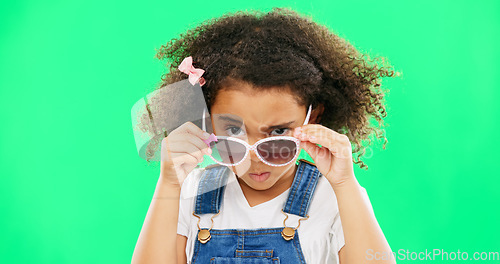 Image of Child, portrait and sunglasses with an attitude on green screen background peeking over glasses. Black girl kid in studio for comic, funny and facial expression or mood while angry or curious