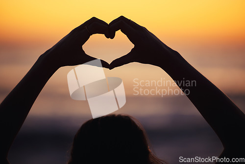 Image of Woman, heart hand and shadow at sunset at beach and ocean with peace and zen hands sign. Silhouette, nature and sea on a vacation with calm meditation and love emoji gesture outdoor at sunrise