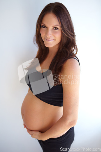 Image of Woman, pregnancy portrait and tummy by wall with smile, excited or pride for new life, future or family. Young mom, pregnant and holding belly with happiness, love or care in house with expectation