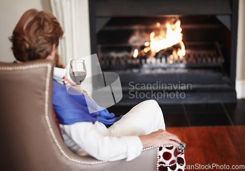 Image of Relax, fire and senior woman with wine, home and comfortable with health, wellness and peace. Back, mature female person or old lady in a lounge, alcohol and warm for winter, weekend break or resting