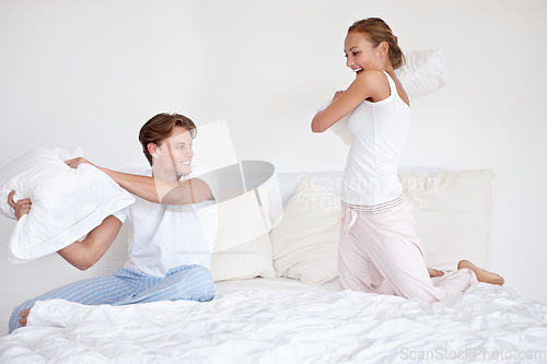 Image of Fun, energy and couple fighting with pillows on the bed in hotel room on a romantic weekend trip. Happy, love and young woman and man laughing, bonding and playing together in the morning in bedroom.