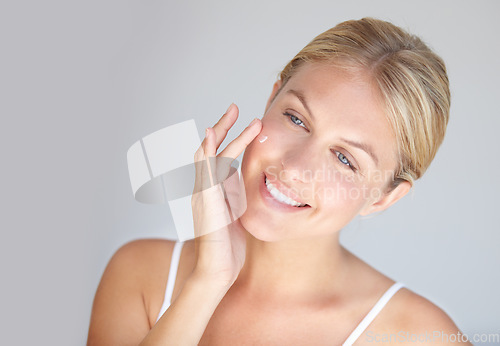 Image of Smile, skincare and woman with cream, cosmetics and dermatology against a grey studio background. Female person, model or girl with lotion, touching face and pamper treatment with grooming and beauty