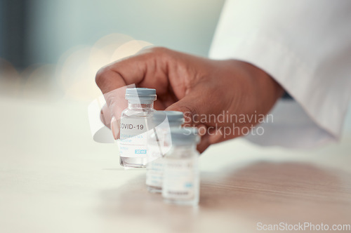 Image of Covid 19, doctor hands and vaccine bottle for virus or corona on table in hospital. Vial, medical professional and person with vaccination, medicine or pharmaceutical drugs for healthcare wellness.