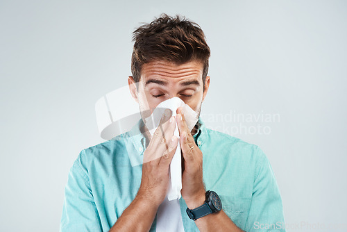 Image of Sick, tissue and face of man blowing nose in studio with flu, illness and virus on white background. Health, wellness and male person with handkerchief for hay fever, cold and sneeze for allergy