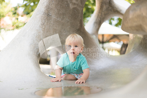 Image of Child playing on outdoor playground. Toddler plays on school or kindergarten yard. Active kid on stone sculpured slide. Healthy summer activity for children. Little boy climbing outdoors.
