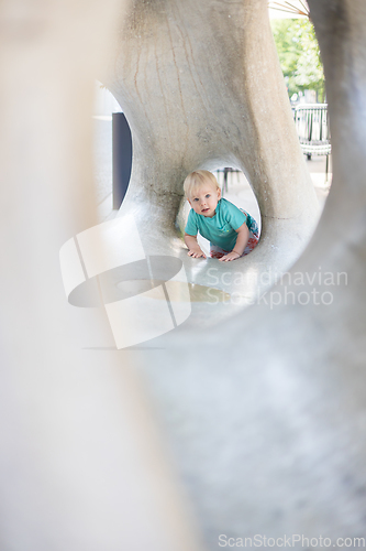 Image of Child playing on outdoor playground. Toddler plays on school or kindergarten yard. Active kid on stone sculpured slide. Healthy summer activity for children. Little boy climbing outdoors.