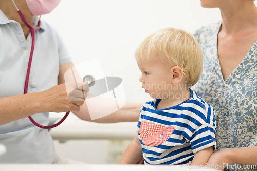 Image of Infant baby boy child being examined by his pediatrician doctor during a standard medical checkup in presence and comfort of his mother. National public health and childs care care koncept.