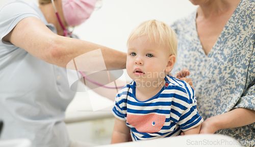 Image of Infant baby boy child being examined by his pediatrician doctor during a standard medical checkup in presence and comfort of his mother. National public health and childs care care koncept.