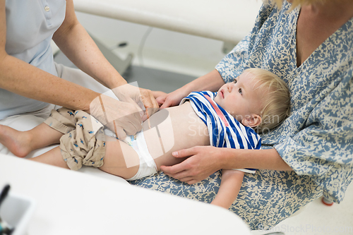 Image of Infant baby boy child being examined by his pediatrician doctor during a standard medical checkup in presence and comfort of his mother. National public health and childs care care koncept.