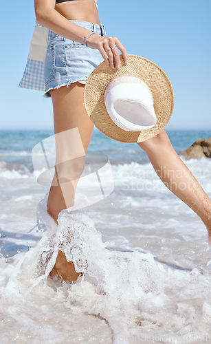 Image of Beach, water and person legs for holiday, vacation or outdoor wellness in summer fashion. Cool, trendy people walking in sea or ocean waves in jeans, hat and clothes for travel, tourism and nature