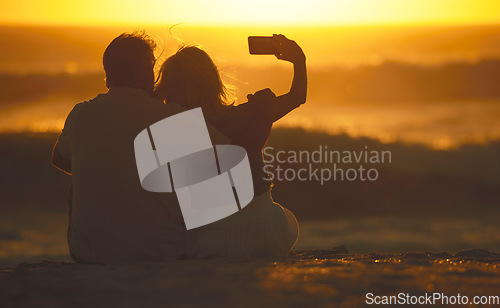 Image of Travel, couple and selfie at sunset on a beach for vacation or holiday outdoor. Behind romantic man and woman in nature with peace, calm and ocean for quality time, love and freedom or photo memory