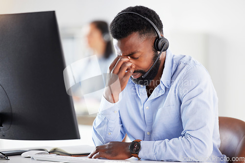 Image of Mental health, man call center agent with headache and headset with computer at his desk in a modern workplace office. Telemarketing or consultant, stress or burnout and male person at workspace