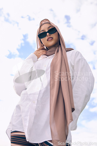 Image of Portrait, fashion and a muslim woman outdoor on a blue sky background in sunglasses and scarf for contemporary style. Islam, faith and hijab with a trendy young arab person outside in modern clothing