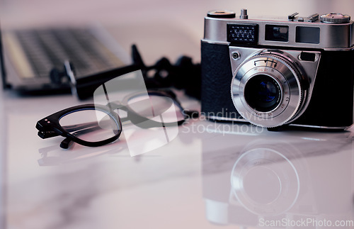 Image of Closeup, desk and photography studio with camera, glasses and computer for art, journalist or news company. Retro equipment, spectacles and professional lens with laptop in office for newspaper job