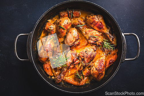 Image of Baked chicken drumsticks with vegetables, casserole dish on black background