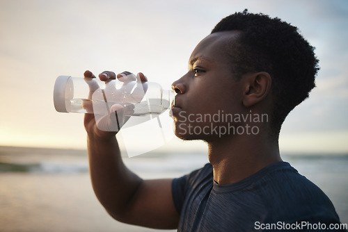 Image of Black man, beach fitness and drinking water at sunset on running break, exercise or workout. Drink, liquid and African male athlete with bottle for nutrition, hydration or health, wellness and ocean.