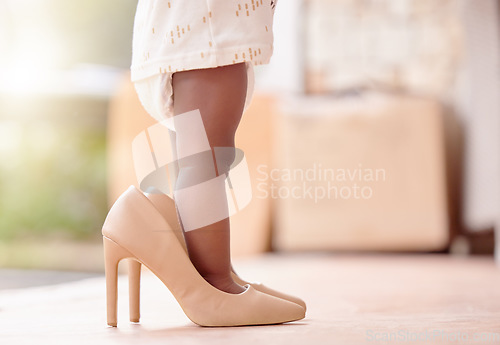 Image of Closeup, baby and girl with high heels shoes in home for childhood growth, toddler and adorable kid. Legs, infant and feet of little child in big footwear for pretend playing, development and walking