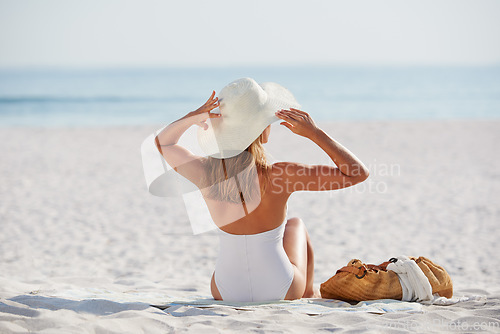 Image of Back, summer and tanning with a woman on the beach to relax during her holiday or vacation at the sea. Nature, ocean and travel with a female tourist sitting on the sand looking at a tropical view